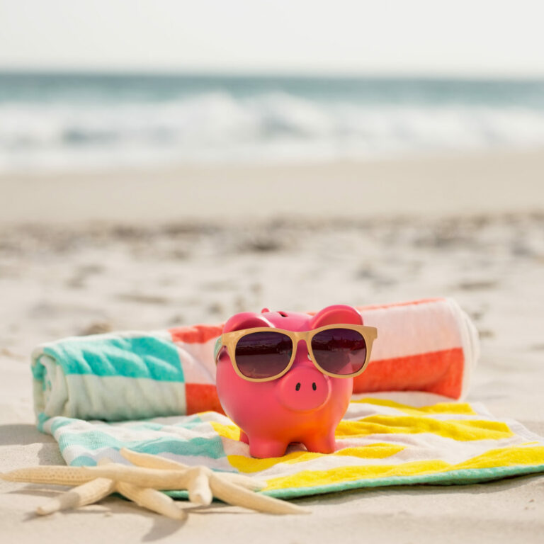 Two starfish and piggy bank with sunglasses on beach blanket