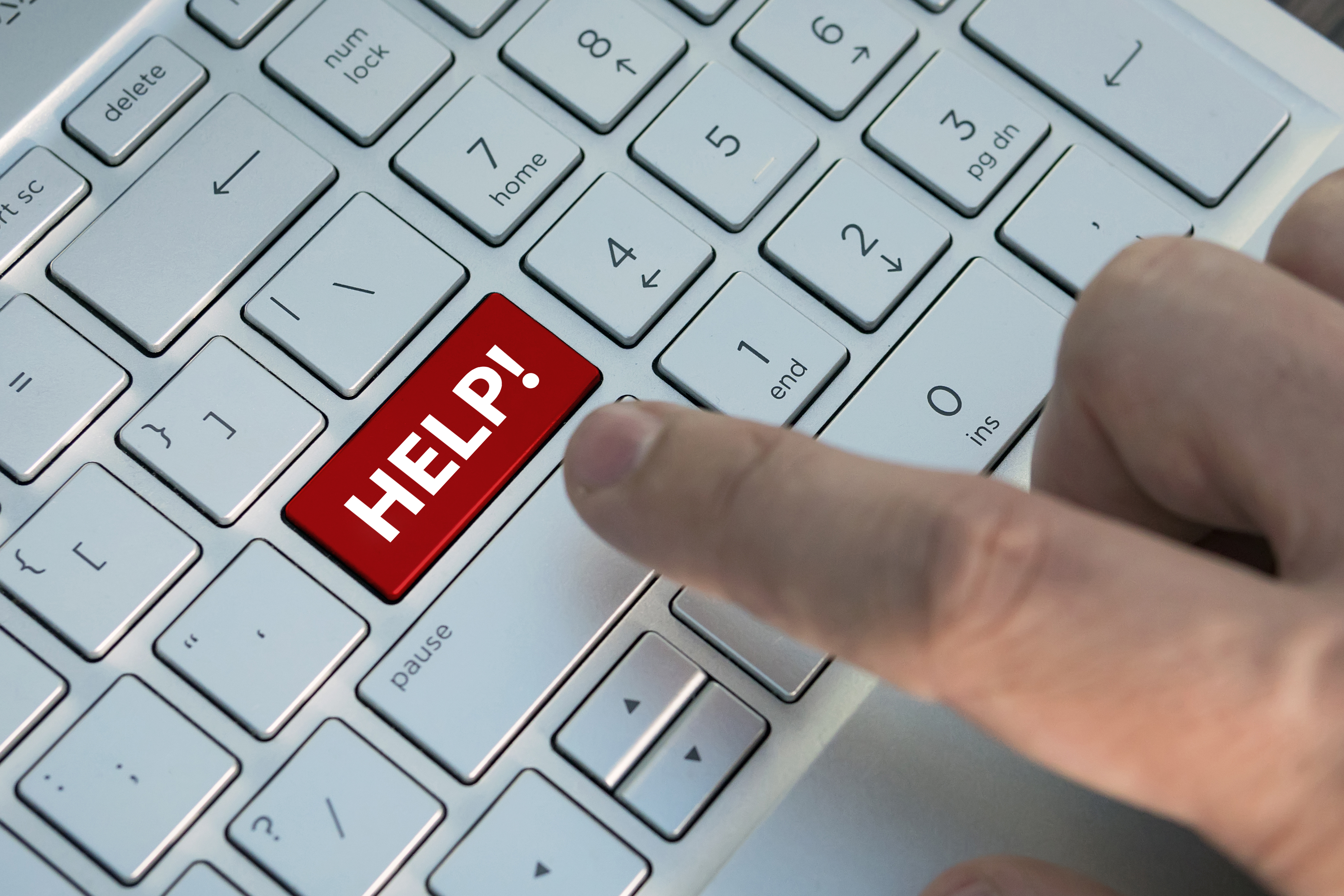 Red help button on the keyboard close-up. A male finger presses a color button on a gray silver keyboard of a modern laptop. Button with inscription close up.